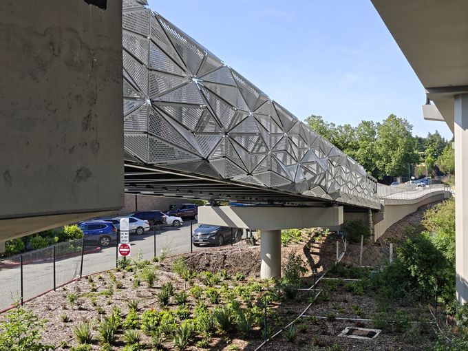 The photo shows one side of a pedestrian bridge, the railing clad in a perforated metal polygon design.